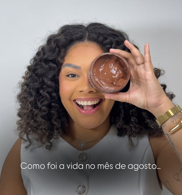 Quezia Machado rindo, segurando um pote de máscara de chocolate na frente de um dos olhos.