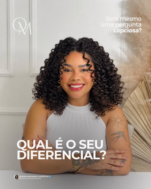 Quezia Machado sorrindo, de cabelo cacheado e blusa branca, com os braços cruzados sobre a mesa.